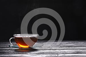 Glass cup of tea and saucer on wooden table against black background, space for text