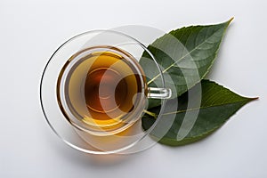 Glass cup with yellow tea and green leaves, plain white background. photo