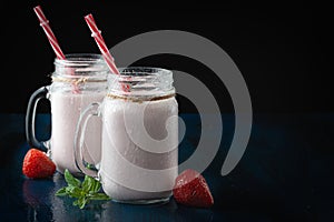 Glass cups with delicious strawberry milkshake on a black table