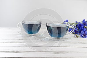 glass cups and teapot of Butterfly pea tea. Anchan  clitoria ternatea on a white wood background. with bouquet of blue flowers