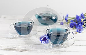 glass cups and teapot of Butterfly pea tea. Anchan on a white marble background. with bouquet of blue flowers