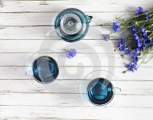 glass cups and teapot of Butterfly pea tea. Anchan on a white wood background. with bouquet of blue flowers