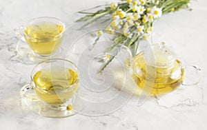 glass cups and teapot with chamomile tea on a white background. a bouquet of daisies