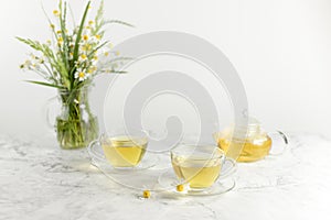 glass cups and teapot with chamomile tea on a white background. a bouquet of daisies