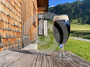 Glass of dark beer on wooden table in the Austrian Alps on a sunny day. Nenzinger Himmel, Vorarlberg, Austria.