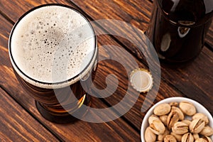 glass of dark cold frothy beer, nuts, bottle, cap, old wooden ta