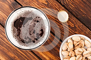 glass of dark cold frothy beer, nuts, bottle cap, old wooden tab