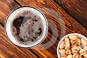 glass of dark cold frothy beer, nuts old wooden table