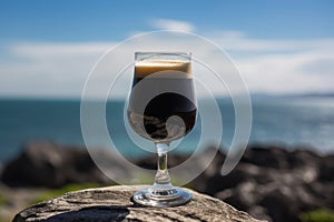 Glass of dark stout beer. Spectacular Irish nature. Green pastures, cliffs and crushing waves. Generative AI