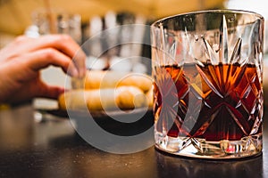 Glass of dark vermouth drink with slice of orange on a bar table outdoors, a popular aperitif, during a summer day with snacks and
