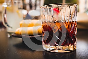 Glass of dark vermouth drink with slice of orange on a bar table outdoors, a popular aperitif, during a summer day with snacks and