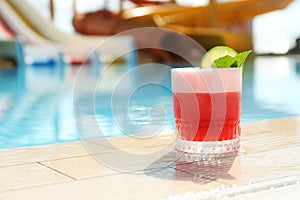 Glass of cocktail near swimming pool, space for text. Refreshing drink