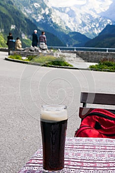 A glass of delicious dark Austrian beer against the backdrop of the European Alps in a restaurant.