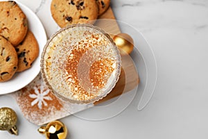 Glass of delicious eggnog with cinnamon and cookies on white table, flat lay. Space for text