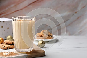 Glass of delicious eggnog with cinnamon and cookies on white table, space for text