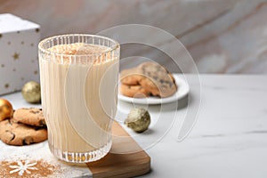 Glass of delicious eggnog with cinnamon on white table, space for text