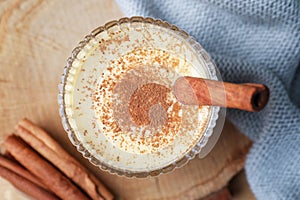 Glass of delicious eggnog with cinnamon on wooden table, flat lay