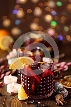 Glass of delicious mulled wine on wooden table against blurred lights