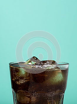 A glass with a drink on a blue background. A glass of cola and ice
