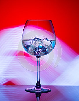 A glass with a drink and ice cubes on a red background