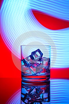 A glass with a drink and ice cubes on a red background