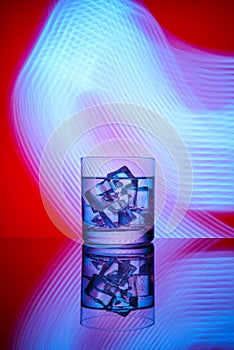 A glass with a drink and ice cubes on a red background