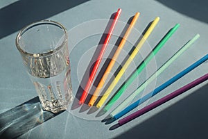 A glass of drinking water with colorful straws for drinking rainbow colors on a blue background, with a shadow pattern