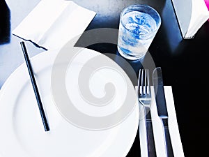 A glass of drinking water filled with ice standing by plate , Knife and fork on the wooden table