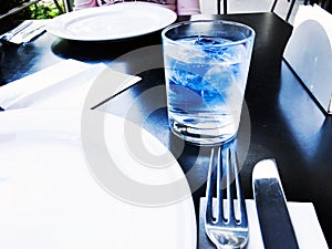 A glass of drinking water filled with ice standing by plate , Knife and fork on the wooden table