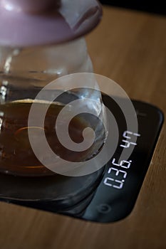 Glass drip pot with black coffee on scales, closeup with blurred background