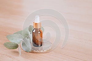 Glass dropper bottle with eucalyptus oil on wooden table background with copy space. Modern organic cosmetics or