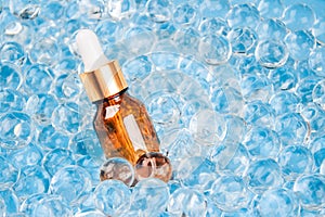 Glass dropper bottle of facial anti aging serum with collagen and peptides on blue gel bubbles background with copy