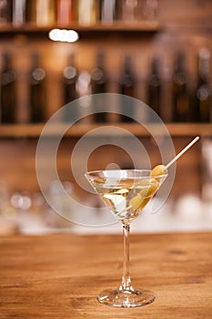 Glass of dry martini with green olives on a rustic wooden bar counter