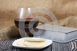 A glass of dry red wine and broken unleavened bread lie on a plate. To celebrate the Lord`s Supper. Nearby lies the Bible