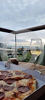 A glass of dry white wine and pepperoni pizza on the balcony