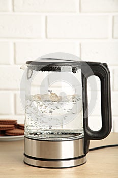 Glass electric kettle with boiling water and chocolate chip cookie on white background