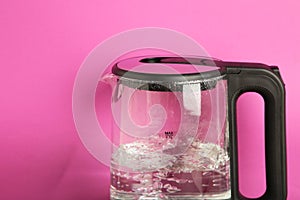 Glass electric kettle with boiling water on pink background