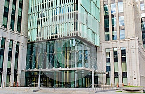 Glass entrance to a modern office building, a tree nearby, blurred cars passing by