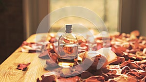 Glass essential oil bottle and roses petals on wooden surface, toned warm, selected focus