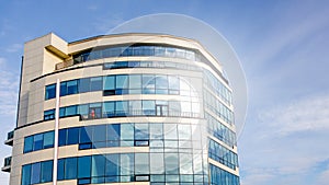 Glass facade of modern multi-storey building with sun glare in windows against blue sky background_