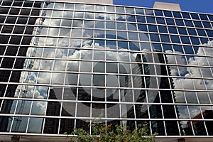 Glass facade of a modern office building with reflections of the cloudy sky.