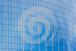 The glass facade of a skyscraper with a mirror reflection of sky windows