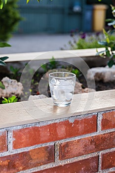 Glass filled with ice and water on a brick wallflower on a terrace. Outside, summer evening. photo