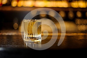 Glass filled with strong cocktail with light whiskey on the bar against the lights