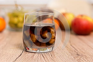A glass filled with sugar cubes and a glass with cola are standing on the table. In the background, mandarin fruits, apples and gr