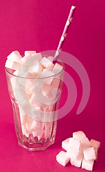 Glass filled with sugar cubes with pink paper straw shows the unhealthy effect of soft drinks