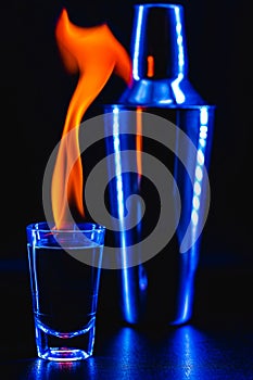 Glass of flaming alcoholic drink, vodka or liquor on fire, black background