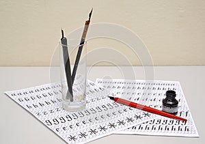 Glass with fountain pens and black ink lie on sheets of calligraphical copy-books