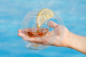 Glass of fragrant cognac with a slice of lemon in a woman`s hand on a blue background