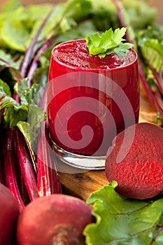 Glass of fresh beetroot juice with bets on wooden table.